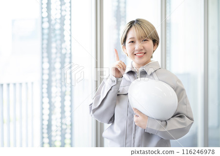 A young woman with short blonde hair wearing work clothes and holding a helmet (pointing, free hair color, working in your own way, work environment) A young woman with short blonde hair wearing work clothes and holding a helmet (pointing, free hair color, working in your own way, work environment) 116246978