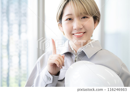 一位身穿工作服、手持頭盔、金髮短髮的年輕女子（指著、自由髮色、以自己的方式工作、工作環境） 116246983