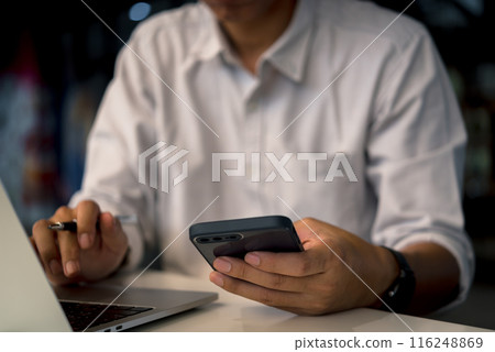 Businessman holding smartphone to communicate work with digital internet, online technology and laptop computer at work desk 116248869