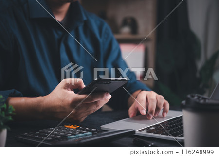 Businessman using smartphone and laptop simultaneously in a modern office setting 116248999