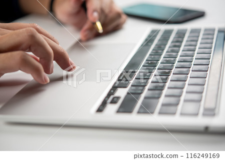 Close-up of hands typing on a laptop keyboard with pen in hand, suggesting business communication Close-up of hands typing on a laptop keyboard with pen in hand, suggesting business communication 116249169