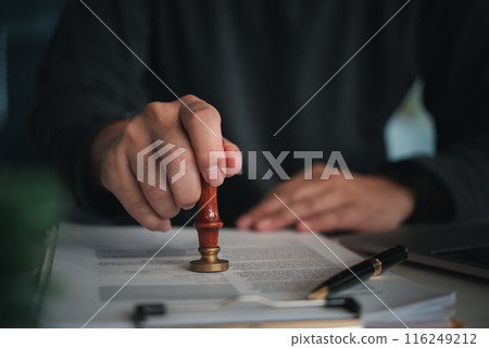 Focused individual placing a seal on an official document with red wax stamp in a professional setting 116249212