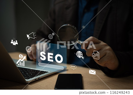 A man is looking at a laptop with a magnifying glass on it 116249243