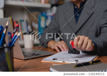 A professional applies an official seal to company documents, signifying authentication and approval. A professional applies an official seal to company documents, signifying authentication and approval. 116249313