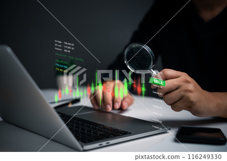 A person examines stock market indicators on a laptop screen using a magnifying glass. The focus on specific data points suggests a detailed analysis of market trends. 116249330