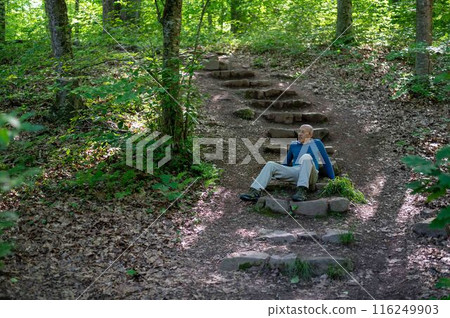 Physically fit senior man sits on woodland hiking trail steps thinking 116249903