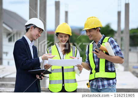 Engineering team discussing over blueprint while standing at construction site Engineering team discussing over blueprint while standing at construction site 116251905