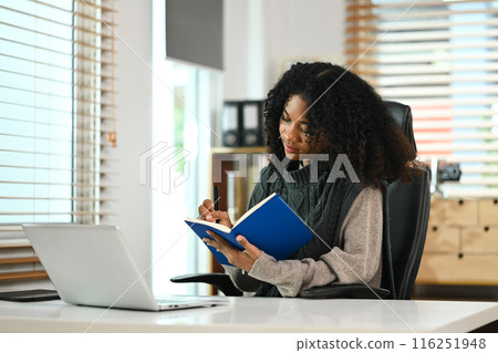 Young African American girl working with laptop and writing on notebook 116251948