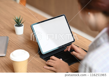 View over shoulder of businesswoman typing on wireless keyboard working with digital tablet at cafe 116251965