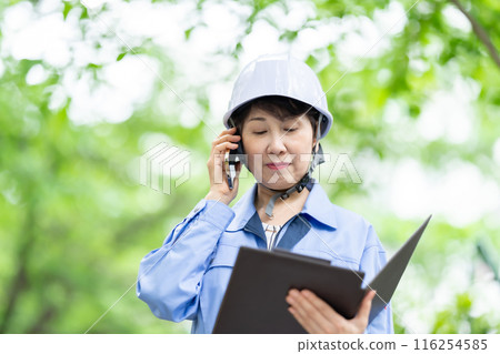 Woman in work clothes, fresh greenery, helmet, smartphone Woman in work clothes, fresh greenery, helmet, smartphone 116254585