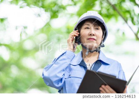 Woman in work clothes, fresh greenery, helmet, smartphone Woman in work clothes, fresh greenery, helmet, smartphone 116254613