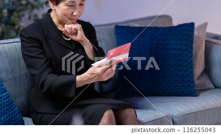 Woman in mourning clothes looking at bankbook, no face 116255043