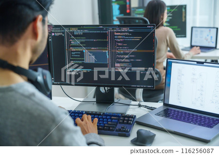 Asian software developers working on multiple screens displaying code and application diagrams in a modern office 116256087