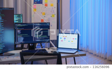 Software development office Workstation setup with multiple monitors displaying code and development diagrams during a nighttime coding session Software development office Workstation setup with multiple monitors displaying code and development diagrams during a nighttime coding session 116256096
