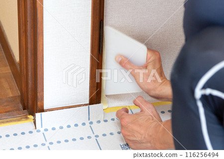 A craftsman replacing wallpaper on a house 116256494