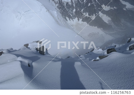 Breathtaking view of a steep snow-covered slope from the towering summit of a majestic mountain peak 116256763