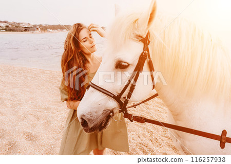 A white horse and a woman in a dress stand on a beach, with the A white horse and a woman in a dress stand on a beach, with the 116257938