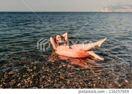 A woman is floating on a pink inflatable raft in the ocean. The water is calm and the sky is clear. The woman is enjoying her time in the water. A woman is floating on a pink inflatable raft in the ocean. The water is calm and the sky is clear. The woman is enjoying her time in the water. 116257959
