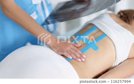 Woman doctor hold scan of woman back and correct kinesiology tape on females body Woman doctor hold scan of woman back and correct kinesiology tape on females body 116257994