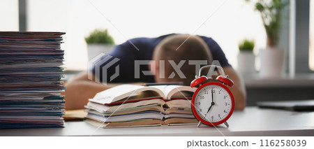 Tired student take nap behind pile of textbooks on table 116258039
