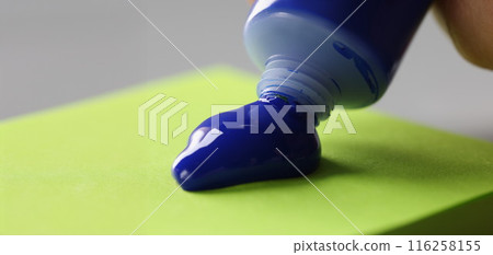 Man artist squeeze paint out of tube, bright blue colour on green paper 116258155