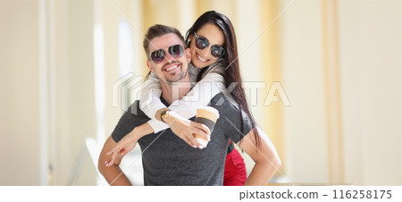Happy couple posing, woman jumped on man back hold cup of coffee Happy couple posing, woman jumped on man back hold cup of coffee 116258175