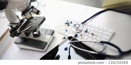Doctor desk with mess and chaos on surface, stethoscope tool, scattered pills on keyboard Doctor desk with mess and chaos on surface, stethoscope tool, scattered pills on keyboard 116258309