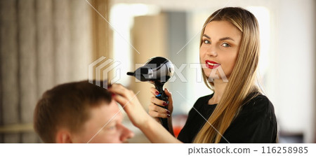 Blonde hairdresser using hairdryer to dry clients hairstyle, new image for man Blonde hairdresser using hairdryer to dry clients hairstyle, new image for man 116258985