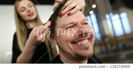 Female professional hairdresser cutting hair with scissors, smiling male client sit in masters chair Female professional hairdresser cutting hair with scissors, smiling male client sit in masters chair 116258989