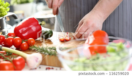 Male chef cutting hot pepper with sharp knife, veggies on cutting board, enjoy cooking 116259020