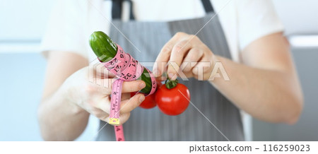 Person hold cucumber and tomatoes with measure tape around, create male organ with vegetables Person hold cucumber and tomatoes with measure tape around, create male organ with vegetables 116259023