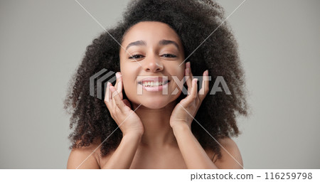 Beauty and healthcare concept - beautiful African American woman with curly afro hairstyle and clean, healthy skin touching face with hand, doing facial massage, posing and looking at camera Beauty and healthcare concept - beautiful African American woman with curly afro hairstyle and clean, healthy skin touching face with hand, doing facial massage, posing and looking at camera 116259798