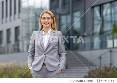 Portrait of a confident businesswoman in a formal suit standing outdoors in front of a modern office building. The woman is smiling, exuding professionalism and success in a corporate environment. Portrait of a confident businesswoman in a formal suit standing outdoors in front of a modern office building. The woman is smiling, exuding professionalism and success in a corporate environment. 116260033