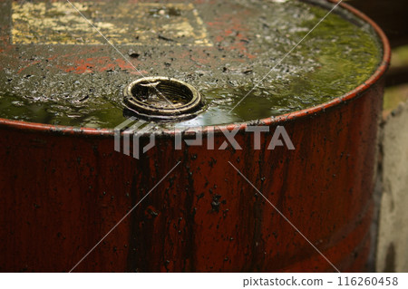 a metal red barrel stands on the street smeared with black liquid, dark oil runs down the barrel 116260458