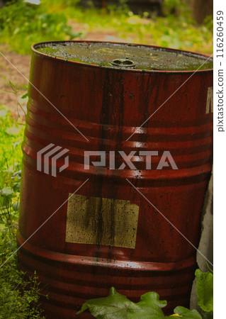 a metal red barrel stands on the street smeared with black liquid, dark oil runs down the barrel 116260459