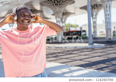 Handsome young african man listen to music via headphones dancing and enjoying his favorite music outdoors on the street. Social media, technology and millennial people concept Handsome young african man listen to music via headphones dancing and enjoying his favorite music outdoors on the street. Social media, technology and millennial people concept 116260700