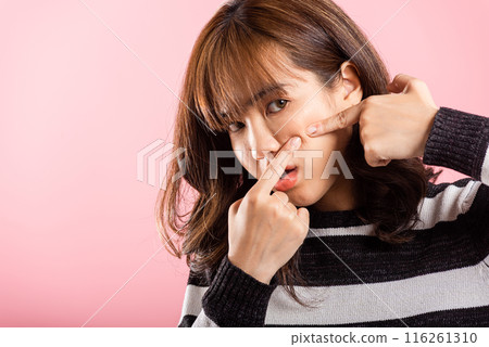 Portrait teenage Asian beautiful young woman having skin problems squeezing pimples acne on her face, studio shot on pink background, with copy space, Thai female acne, beauty care concept 116261310