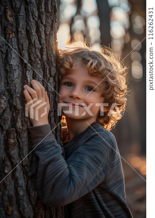 Selective focus of A Caucasian boy hugs the trunk of a big tree in the forest with a happy smile. 116262431