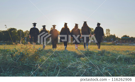 College graduates walk at sunset holding hands. College graduates walk at sunset holding hands. 116262906