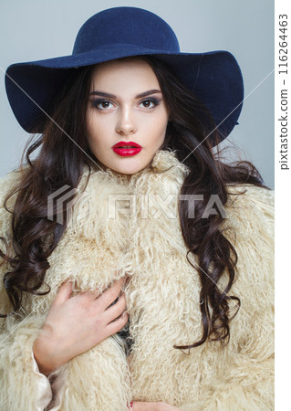 Glamorous young brunette lady with makeup and long curly hair posing on blue background Glamorous young brunette lady with makeup and long curly hair posing on blue background 116264463