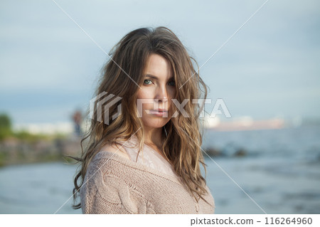Nice young adult woman with natural make-up and long wavy brown hair on blue sea beach 116264960