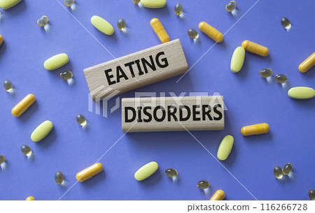 Eating Disorders symbol. Concept word. Eating Disorders on wooden blocks. Beautiful purple background with pills. Medicine and Eating Disorders concept. Copy space 116266728