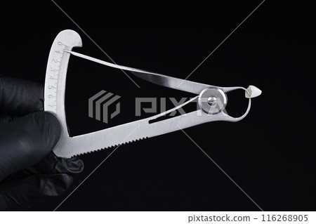 Micrometer measures the thickness of a high-quality zirconia crown. Black background. Micrometer measures the thickness of a high-quality zirconia crown. Black background. 116268905