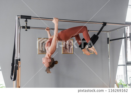 Pilates fitness trainer doing back strengthening exercises on in pilates studio. Balanced Body Cadillac machine for fitness workouts in gym. Fit, healthy and strong authentical body. Fitness concept. 116269162