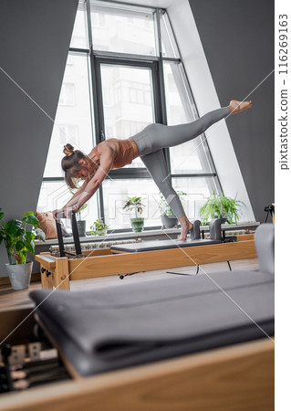 Woman doing Pilates exercise for core and back muscles on Reformer machine with determination and focus on strength body 116269163