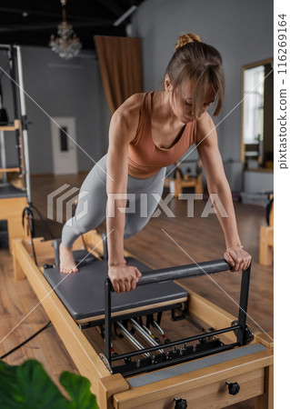 Woman doing Pilates exercise for core and back muscles on Reformer machine with determination and focus on strength body 116269164