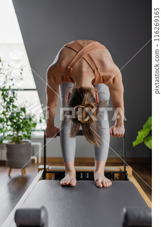 Woman doing Pilates exercise for core and back muscles on Reformer machine with determination and focus on strength body 116269165