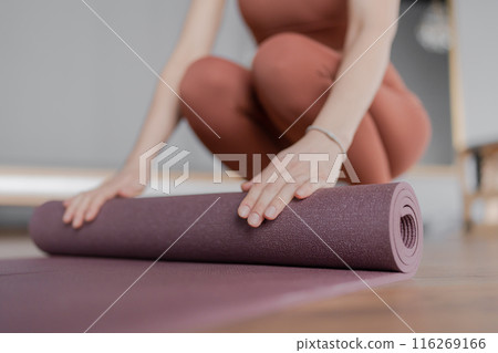 Woman trainer rolling out a mat after class. Rolled yoga mats in a studio create a peaceful atmosphere for meditation and exercise. Woman trainer rolling out a mat after class. Rolled yoga mats in a studio create a peaceful atmosphere for meditation and exercise. 116269166