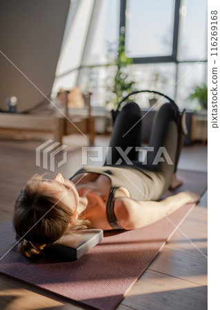 A woman is using a hip Magic Circle at Glute bridge Pilates workout in studio, being active and committed to exercising 116269168
