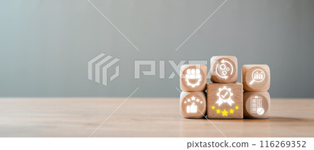 Wooden blocks with icons symbolizing quality management, business excellence, and continuous improvement on a wooden table with a grey background. 116269352